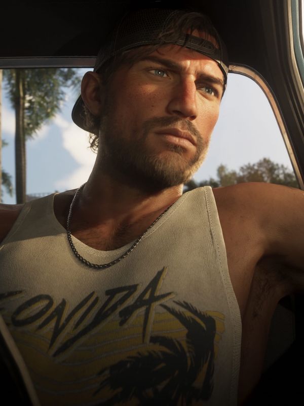 Jason Duval, in a baseball cap and white tank top, sitting in the driver's seat of a car and looking out of the window.