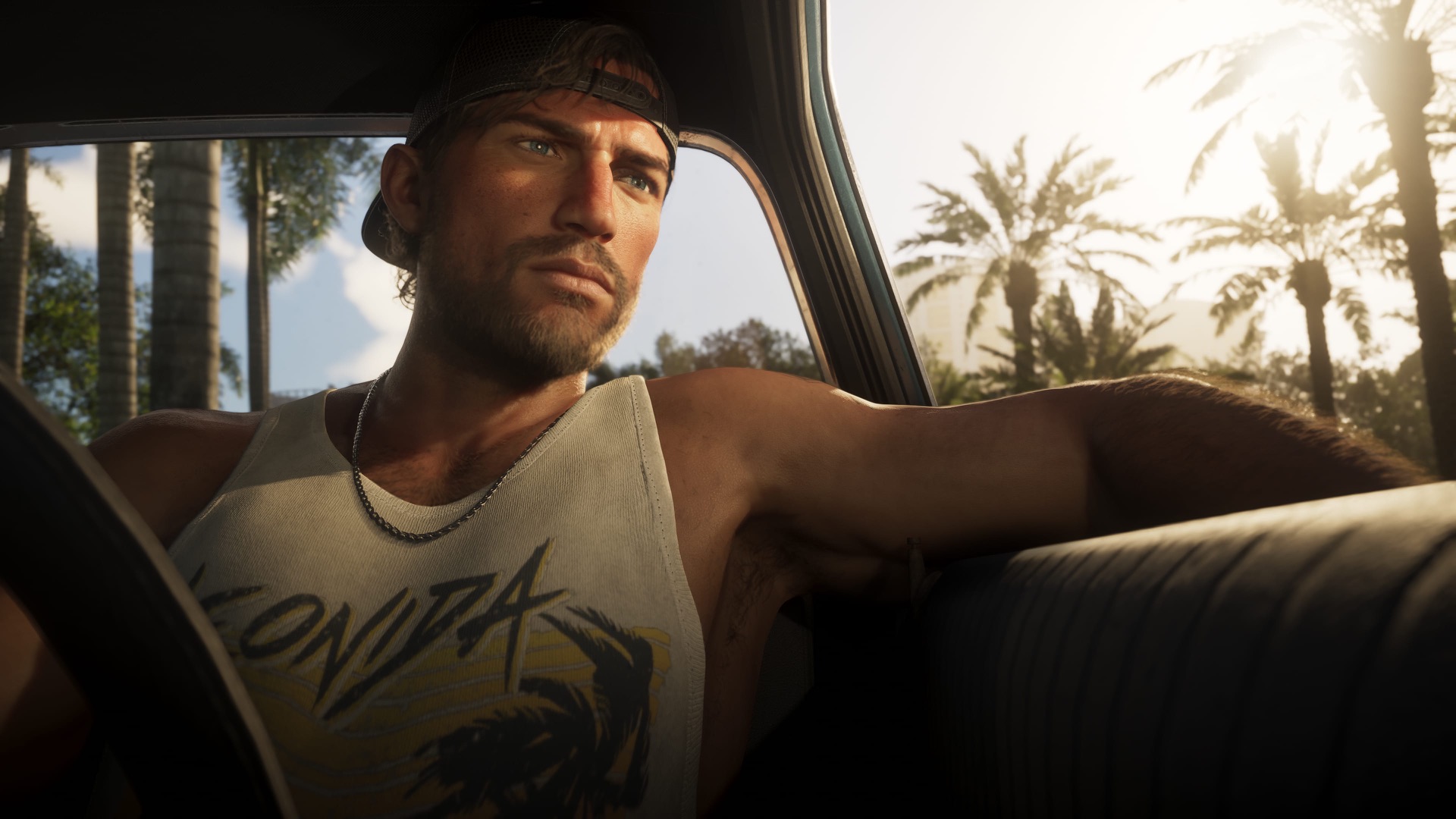 Jason Duval, in a baseball cap and white tank top, sitting in the driver's seat of a car and looking out of the window.