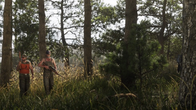 Two men carrying rifles, one in camouflage overalls and one in an orange tank top, walking through tall grass in a pine forest.
