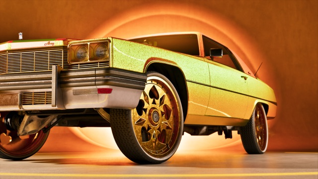 A metallic gold car with a chrome grille sits on oversized gold rims in an orange-lit studio.