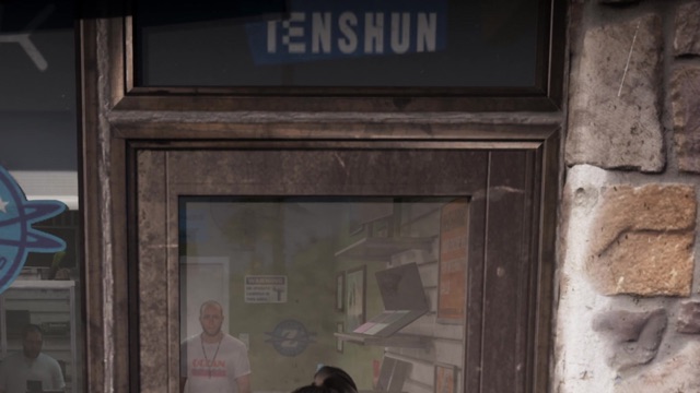 A Tenshun sign in the window of a gadget store, beside a stone wall.