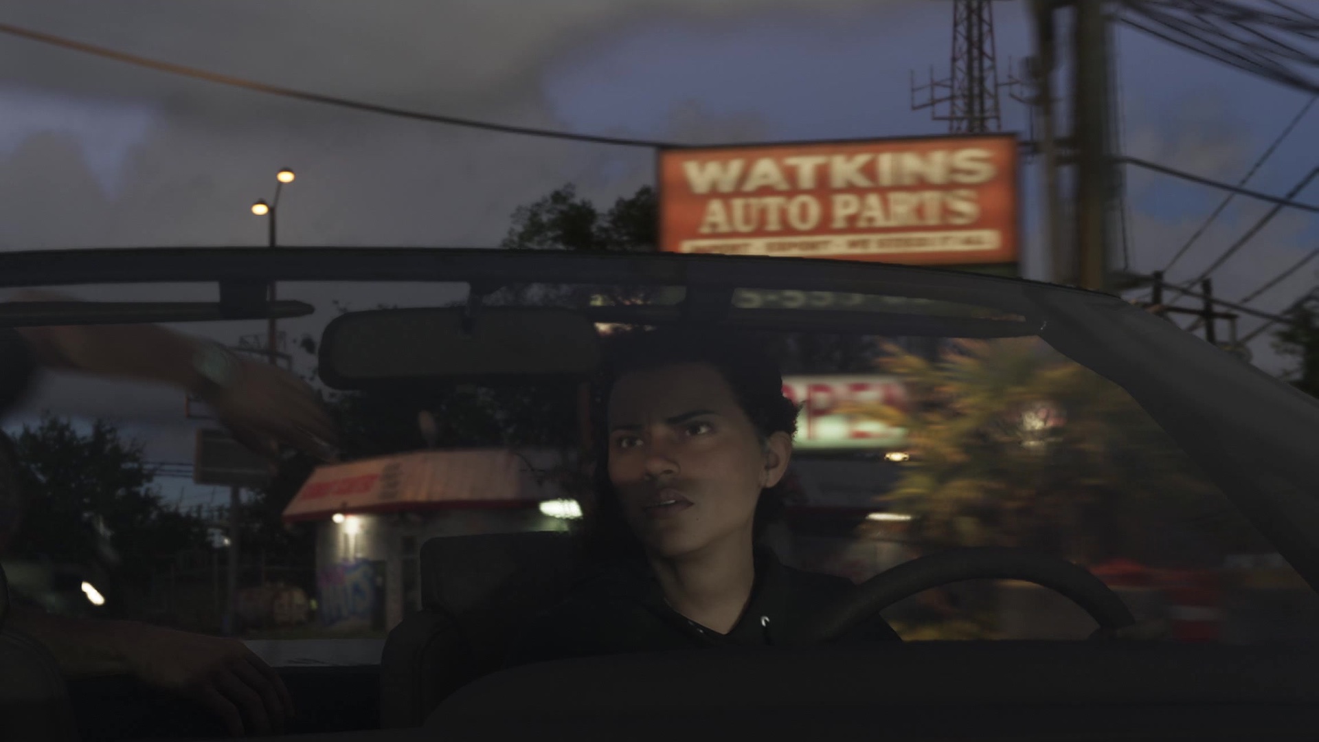 A woman drives at dusk under an orange Watkins Auto Parts sign.